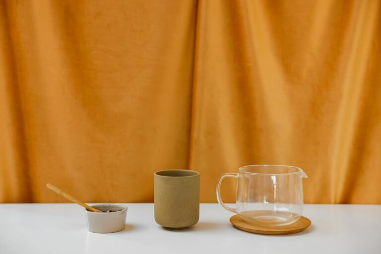 Simple arrangement of ceramic cup, glass pitcher, and bowl against yellow backdrop